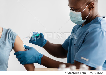 Adult african american doctor in protective mask, gloves and uniform vaccinated patient in clinic 75974664