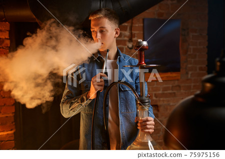 Young man blows smoke in hookah bar, hooka Young man blows smoke in hookah bar, hooka 75975156