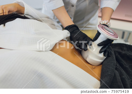 Woman in special white suit getting anti cellulite massage in a spa salon. LPG, and body contouring treatment in clinic. Woman in special white suit getting anti cellulite massage in a spa salon. LPG, and body contouring treatment in clinic. 75975419