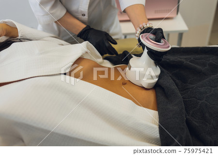 Woman in special white suit getting anti cellulite massage in a spa salon. LPG, and body contouring treatment in clinic. 75975421