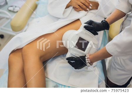 Woman in special white suit getting anti cellulite massage in a spa salon. LPG, and body contouring treatment in clinic. Woman in special white suit getting anti cellulite massage in a spa salon. LPG, and body contouring treatment in clinic. 75975423