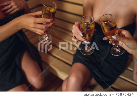 people, beauty, lifestyle, holidays and relaxation concept - beautiful young woman in white bath robe lying on chaise-longue and drinking champagne at spa . people, beauty, lifestyle, holidays and relaxation concept - beautiful young woman in white bath robe lying on chaise-longue and drinking champagne at spa . 75975424