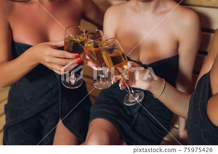 people, beauty, lifestyle, holidays and relaxation concept - beautiful young woman in white bath robe lying on chaise-longue and drinking champagne at spa . people, beauty, lifestyle, holidays and relaxation concept - beautiful young woman in white bath robe lying on chaise-longue and drinking champagne at spa . 75975426
