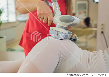 Woman in special white suit getting anti cellulite massage in a spa salon. LPG, and body contouring treatment in clinic. 75975941