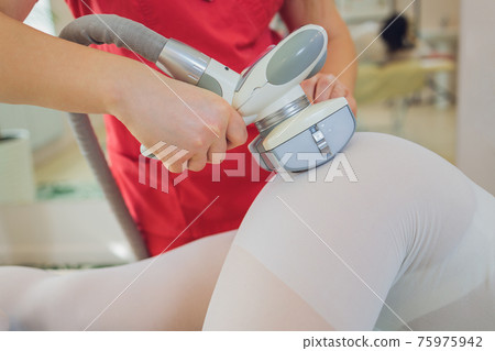 Woman in special white suit getting anti cellulite massage in a spa salon. LPG, and body contouring treatment in clinic. 75975942