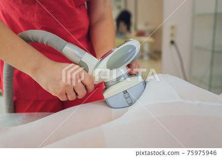 Woman in special white suit getting anti cellulite massage in a spa salon. LPG, and body contouring treatment in clinic. Woman in special white suit getting anti cellulite massage in a spa salon. LPG, and body contouring treatment in clinic. 75975946