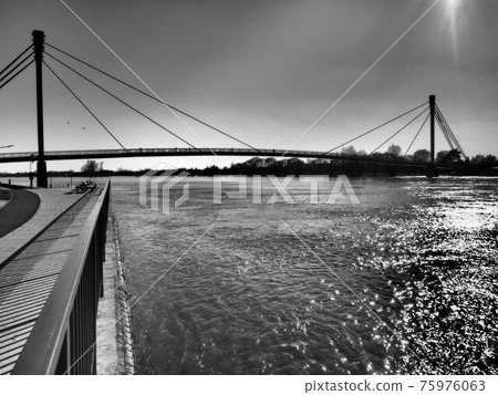 Bridge over the Sava river in Sremska Mitrovica, Serbia. Black and white monochrome photography in retro and vintage style. Reflections of rays on the water. Full-flowing river. Sun in the sky. Bridge over the Sava river in Sremska Mitrovica, Serbia. Black and white monochrome photography in retro and vintage style. Reflections of rays on the water. Full-flowing river. Sun in the sky. 75976063