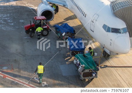 The tractor pulls the carts with luggage to the air plane. The tractor pulls the carts with luggage to the air plane. 75976107