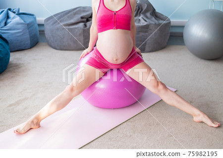 Cropped view of unrecognizable pregnant woman in yoga class. Future mother faceless with a bare tummy is engaged in fitness with a ball. Cropped view of unrecognizable pregnant woman in yoga class. Future mother faceless with a bare tummy is engaged in fitness with a ball. 75982195