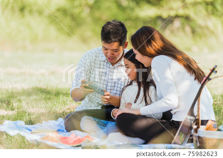 Happy family having fun outdoor sitting on picnic blanket taking selfie 75982623