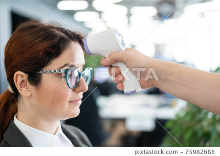 Temperature measurement by electronic infrared thermometer for office staff. Sick woman in a suit. Checking the operation of the gun-thermometer is non-contact. Prevention of the spread of covid-19. 75982688