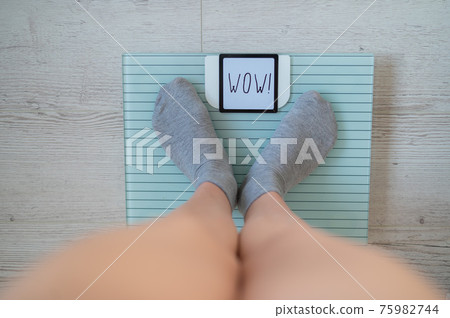 Top view of female legs in gray socks on electronic scales. The inscription on the display is wow. 75982744