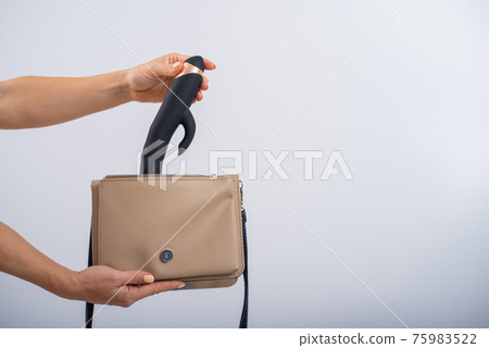 A woman puts a dildo in a handbag on a white... - Stock Photo [75983522]