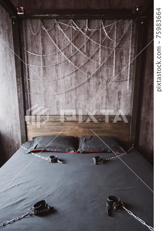 Bedroom for intimate meetings. VDSM equipment and sex toys. Leather handcuffs with a chain on a gray sheet. Fifty shades of gray. Fetish domination. Bedroom for intimate meetings. VDSM equipment and sex toys. Leather handcuffs with a chain on a gray sheet. Fifty shades of gray. Fetish domination. 75983664