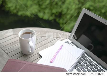 Coffee, notepad, book, pen and computer laptop on table with green plants at the background. Coffee, notepad, book, pen and computer laptop on table with green plants at the background. 75983693