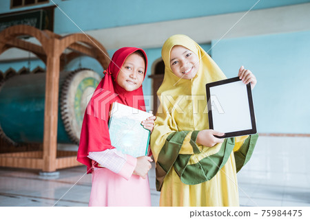 two kid girl Muslim smiling holding blank tablet and al quran book 75984475