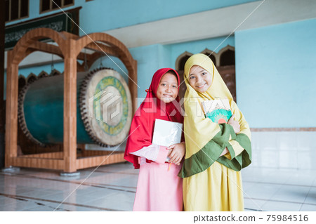 two smiling Muslim girls holding al quran book in their hands two smiling Muslim girls holding al quran book in their hands 75984516
