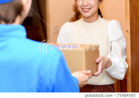 A young woman receiving luggage (courier) from a worker at the entrance 75984565