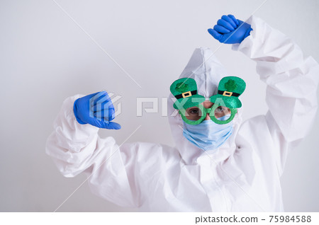 A woman in a protective suit and a medical mask and wearing funny glasses celebrates st patrick's day A woman in a protective suit and a medical mask and wearing funny glasses celebrates st patrick's day 75984588