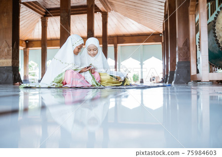 two Asian Muslim girls reading and studying the holy book of the Al-Quran together sitting on the floor 75984603
