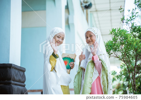 two Asian Muslim girls wearing mukena holding al quran book after salat together and wave hand to camera 75984605