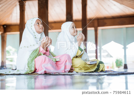 two Asian Muslim girls together sitting on the floor worship and prays for Allah 75984611