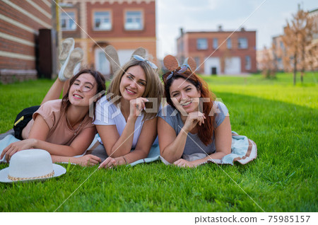 Three beautiful Caucasian young women lie on the lawn in the countryside. The blonde brunette and the redhead are resting in the park on the green grass. The friends had an outdoor picnic. Three beautiful Caucasian young women lie on the lawn in the countryside. The blonde brunette and the redhead are resting in the park on the green grass. The friends had an outdoor picnic. 75985157