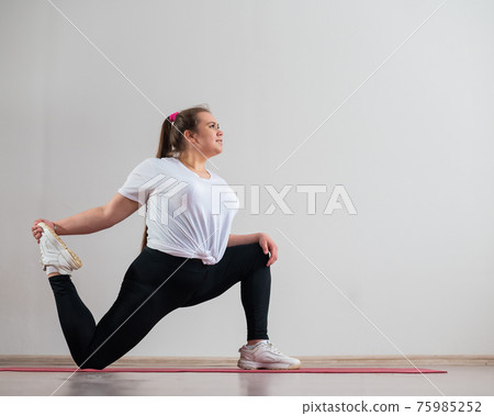Young fat woman doing flexibility exercises on a white background 75985252