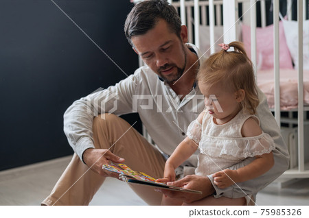 A caring father reads a fairy tale to his little daughter in the children's bedroom. A caring father reads a fairy tale to his little daughter in the children's bedroom. 75985326