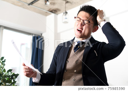 A businessman man who is shocked while holding his head 75985390