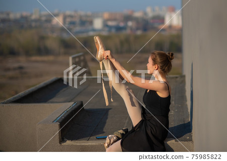 Ballerina in a tutu posing near the fence. Beautiful young woman wearing a black dress and wearing pointe shoes outside. Gorgeous ballerina demonstrates amazing stretching. Ballerina in a tutu posing near the fence. Beautiful young woman wearing a black dress and wearing pointe shoes outside. Gorgeous ballerina demonstrates amazing stretching. 75985822