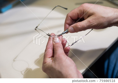 Optical technician fixing glasses. Close-up of male hands with screwdriver and goggles frame. Optical technician fixing glasses. Close-up of male hands with screwdriver and goggles frame. 75986518