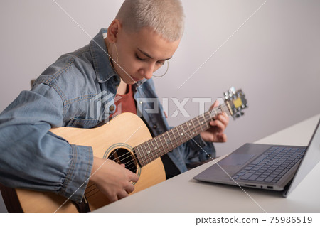Young woman is learning to play the guitar online. Remote music lessons on a laptop 75986519