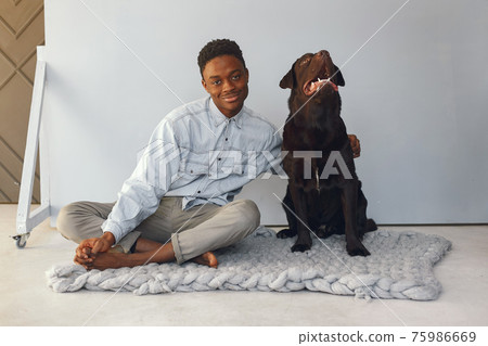 Handsome black man sitting on a blue background with a dog 75986669