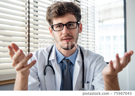 Young male doctor explaining and talking with patient online via video calling Young male doctor explaining and talking with patient online via video calling 75987043