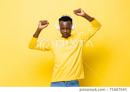 Young African man listening to music with headphones closing eyes and dancing Young African man listening to music with headphones closing eyes and dancing 75987045