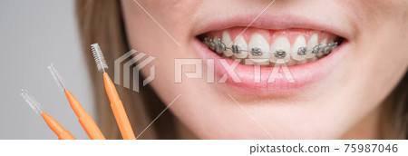 Close-up portrait of a woman with braces on her teeth holding a brush. 75987046