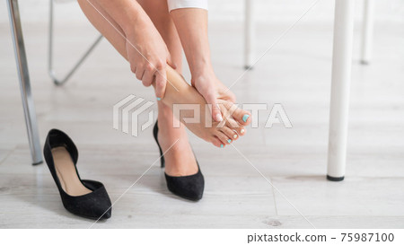 A business woman sits in an office on a chair, takes off her high-heeled shoes and massages her tired feet 75987100