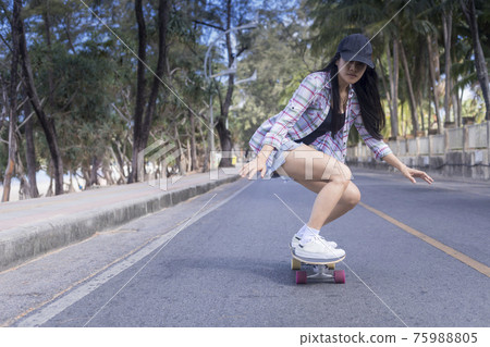 Young asian women play surf skate board at beach road outdoors on morning. Happy women play surfskate board on beach road . Sport activity lifestyle concept 75988805