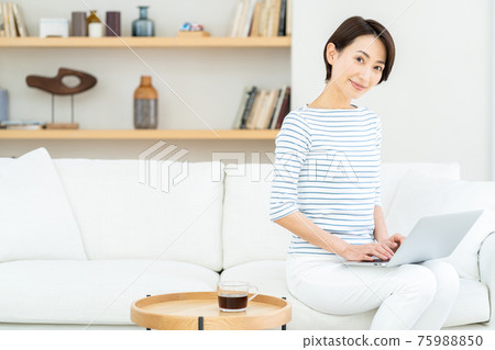 A middle-aged woman teleworking in the living room. 75988850