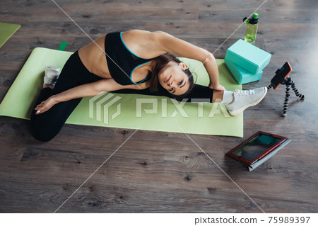 Young woman practicing yoga, is engaged with the teacher online. 75989397