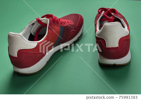 Pair of new red sneakers on a green background. Casual shoes. Space for text. 75991383