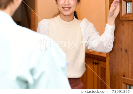 一個穿著工作服的人要拜訪，一個年輕的女人在入口處開門 75991895