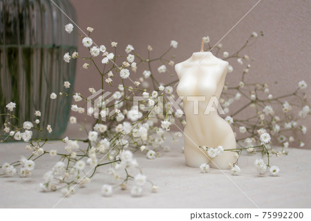 Candle figure of a woman on a table with a vase of white flowers 75992200