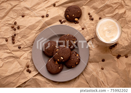 Baked dark Chocolate chip cookies on a plate with glass of coffee on brown paper background Baked dark Chocolate chip cookies on a plate with glass of coffee on brown paper background 75992202