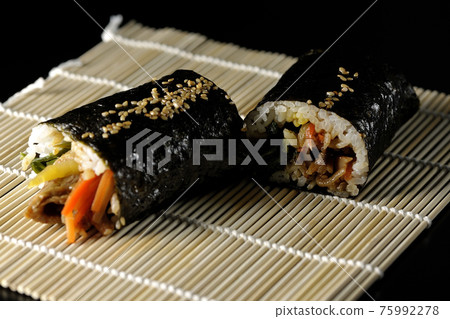 A thick roll on a makisu, a gimbap shot on a black background A thick roll on a makisu, a gimbap shot on a black background 75992278