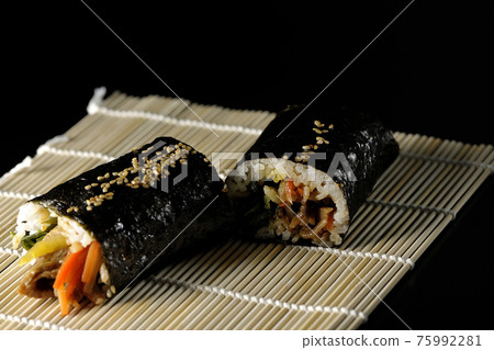 A thick roll on a makisu, a gimbap shot on a black background 75992281