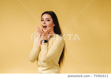 Happy surprised woman in yellow sweatshirt posing to photographer. Portrait of pretty woman on gray background 75992611