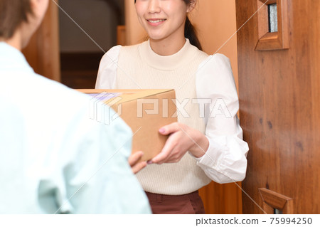A young woman receiving luggage (courier) from a worker at the entrance 75994250