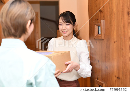 A young woman receiving luggage (courier) from a worker at the entrance A young woman receiving luggage (courier) from a worker at the entrance 75994262